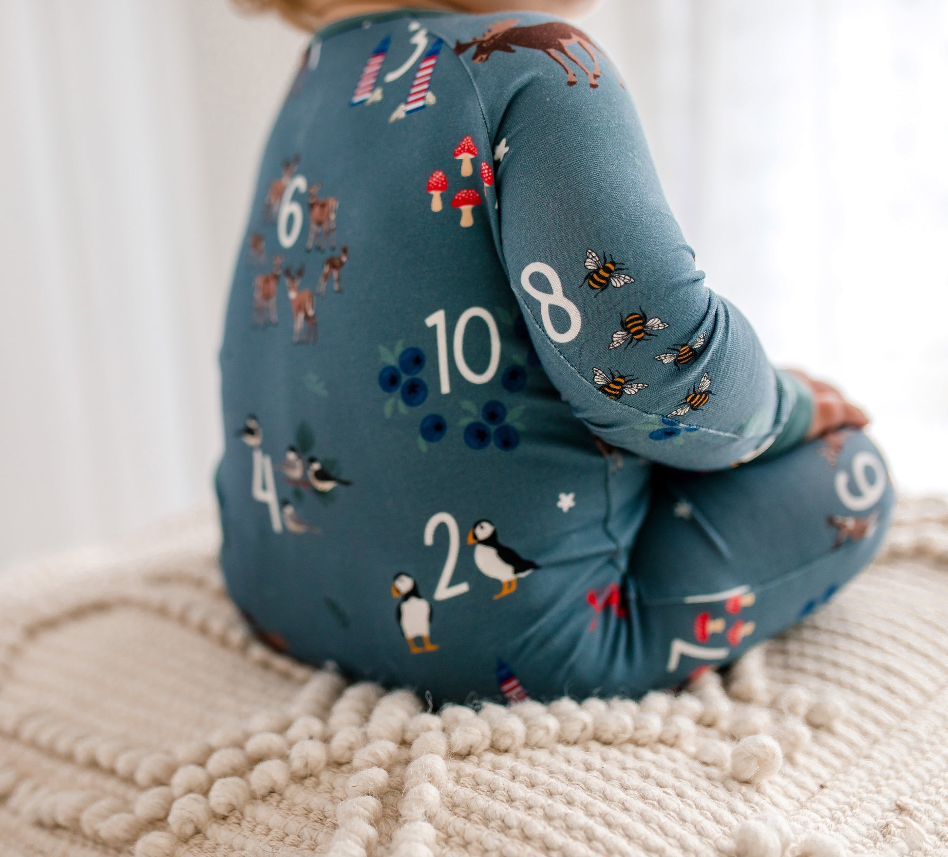 Child wearing a gray one piece with numbers, animals, lighthouses, blueberries, and moose. 