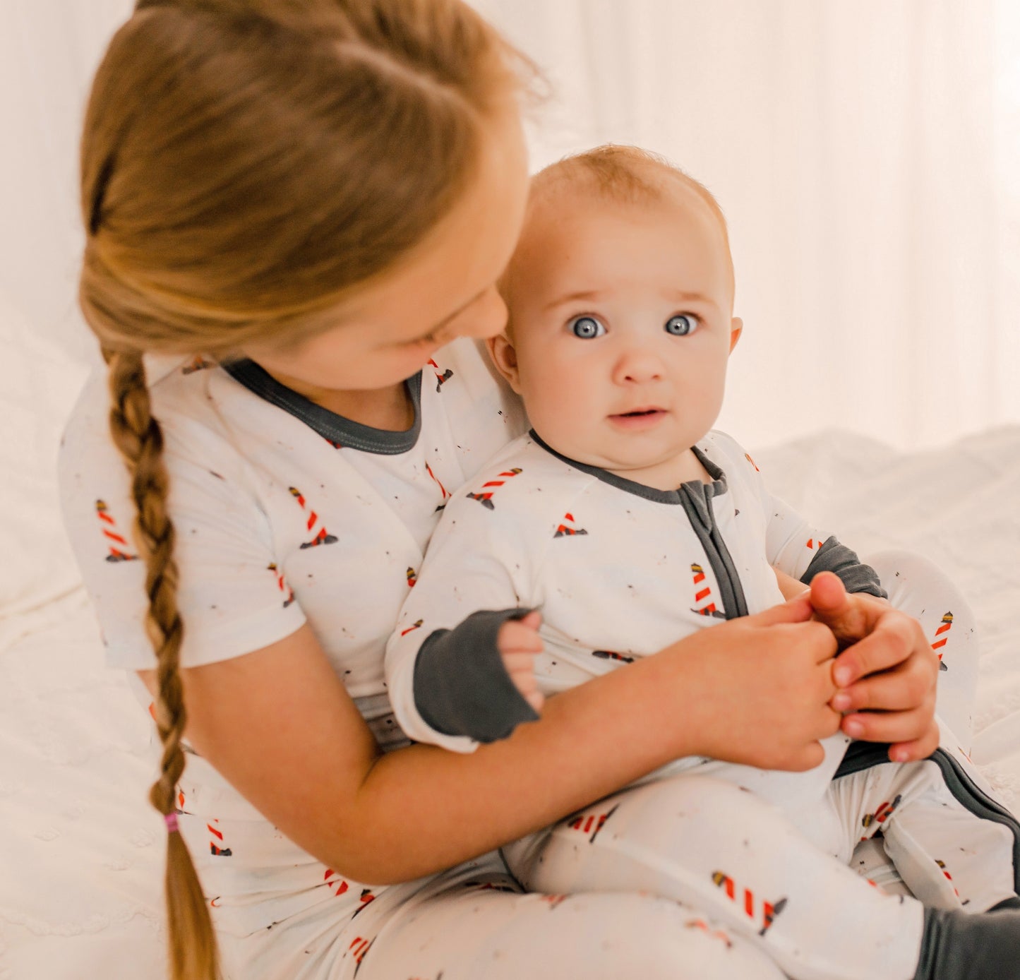 Two children in matching pajamas of Maine Lighthouses that are red and white with black accents 