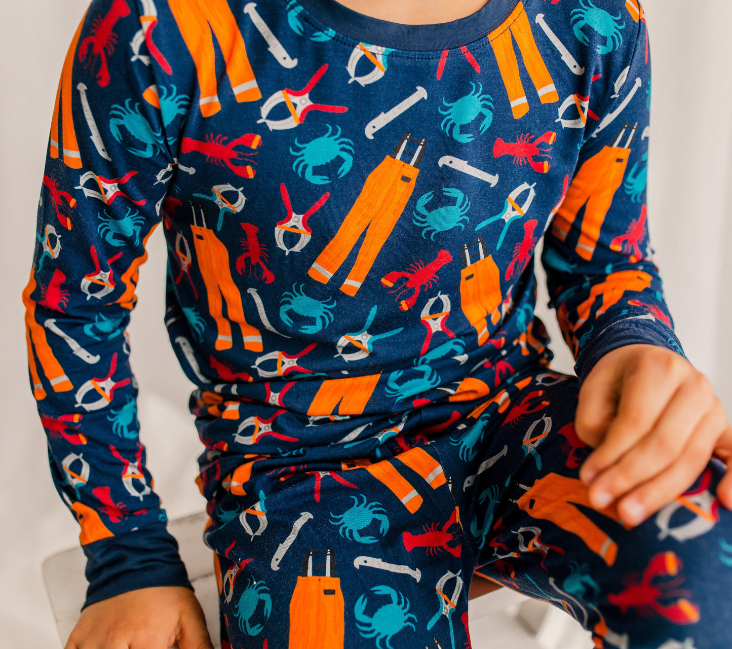 Child wearing long sleeved pajamas with oil gear, ocean animals like crabs and lobsters, and tools for working on a lobster boat 