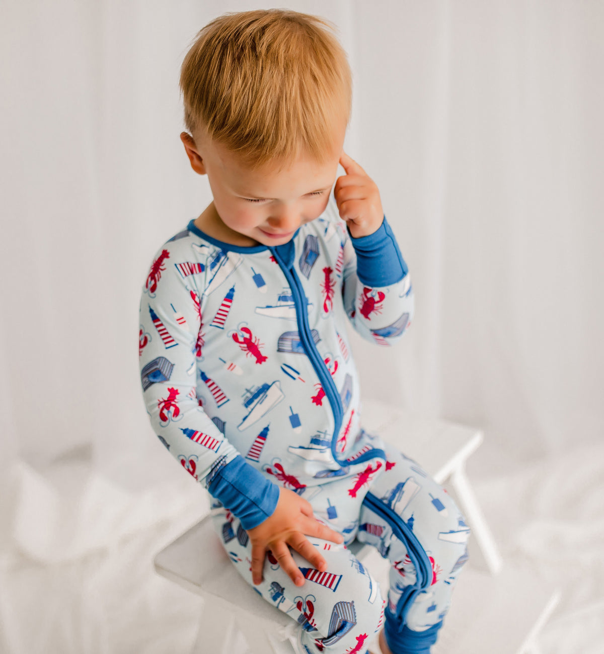 Child wearing pajamas with a lobster pattern, boats, lighthouses, buoys, and traps. 