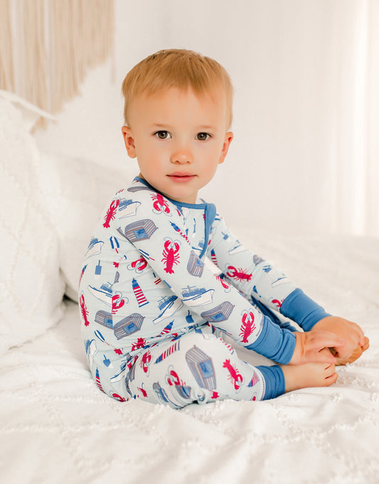 Child wearing pajamas with a lobster pattern, boats, lighthouses, buoys, and traps. 