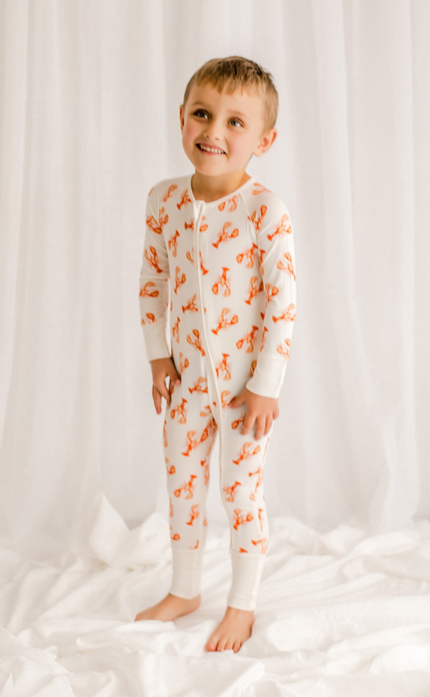 Child wearing a white one piece with orange lobster patterns on a white background