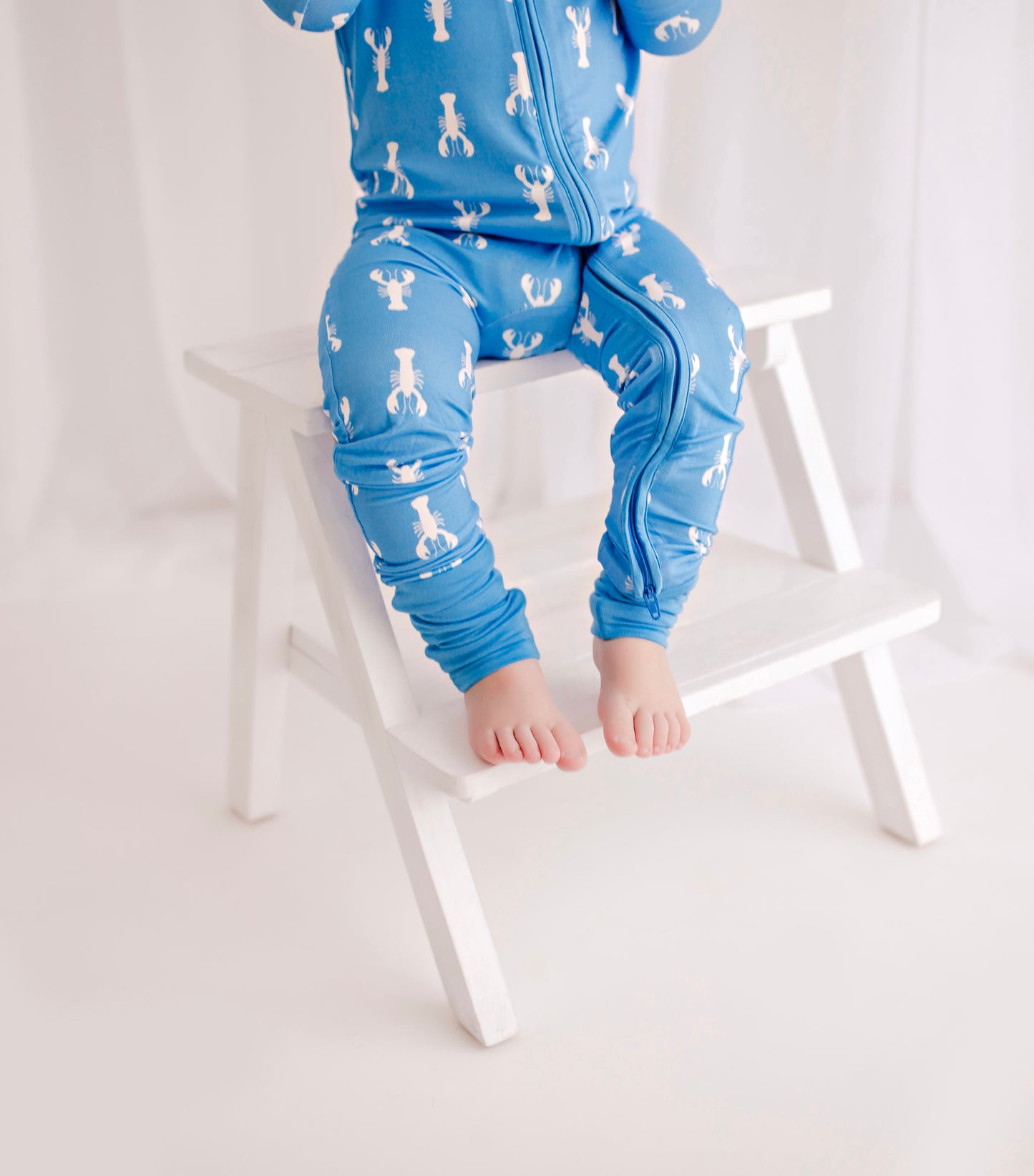 Child wearing baby blue zippy romper with white lobster pattern 