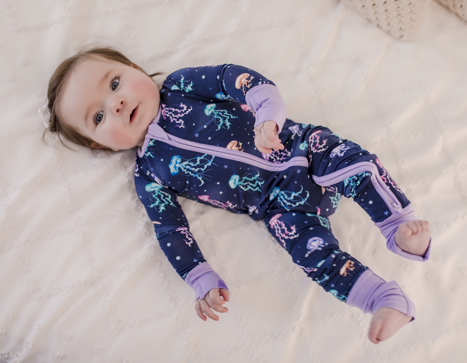 Baby wearing colorful jellyfish themed pajamas with tiny stars and circles with purple cuffs 