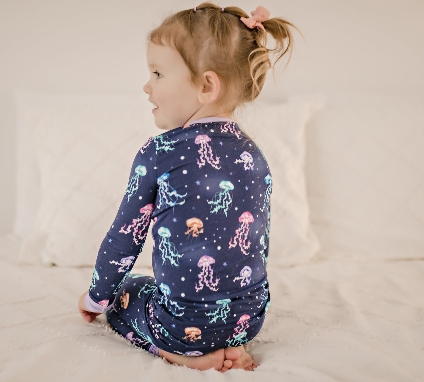 Child wearing dark blue two piece pajama set with colorful jellyfish all over with purple cuffs 