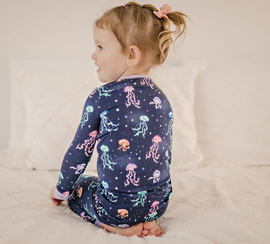 Child wearing dark blue two piece pajama set with colorful jellyfish all over with purple cuffs 