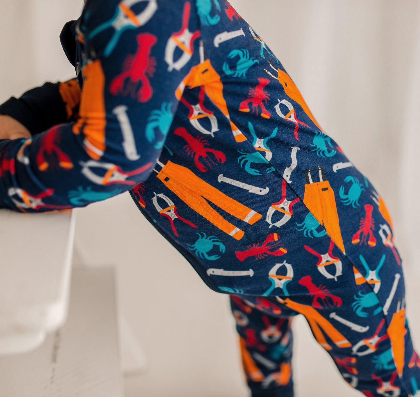Colorful patterned one piece pajama with lobsters, crabs, and oil pants on a navy background 