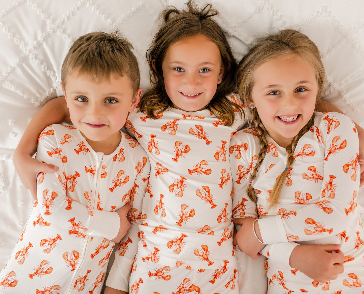Three children wearing matching pajamas with orange maine lobster patterns