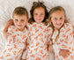 Three children wearing matching pajamas with orange maine lobster patterns