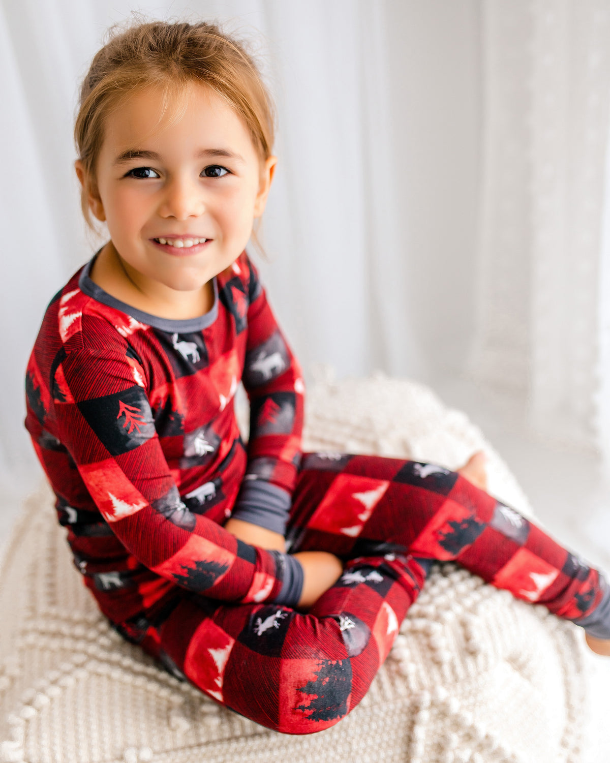 Child wearing red and black checkered pajamas with different types of maine trees and one of maine's icons, the moose. 