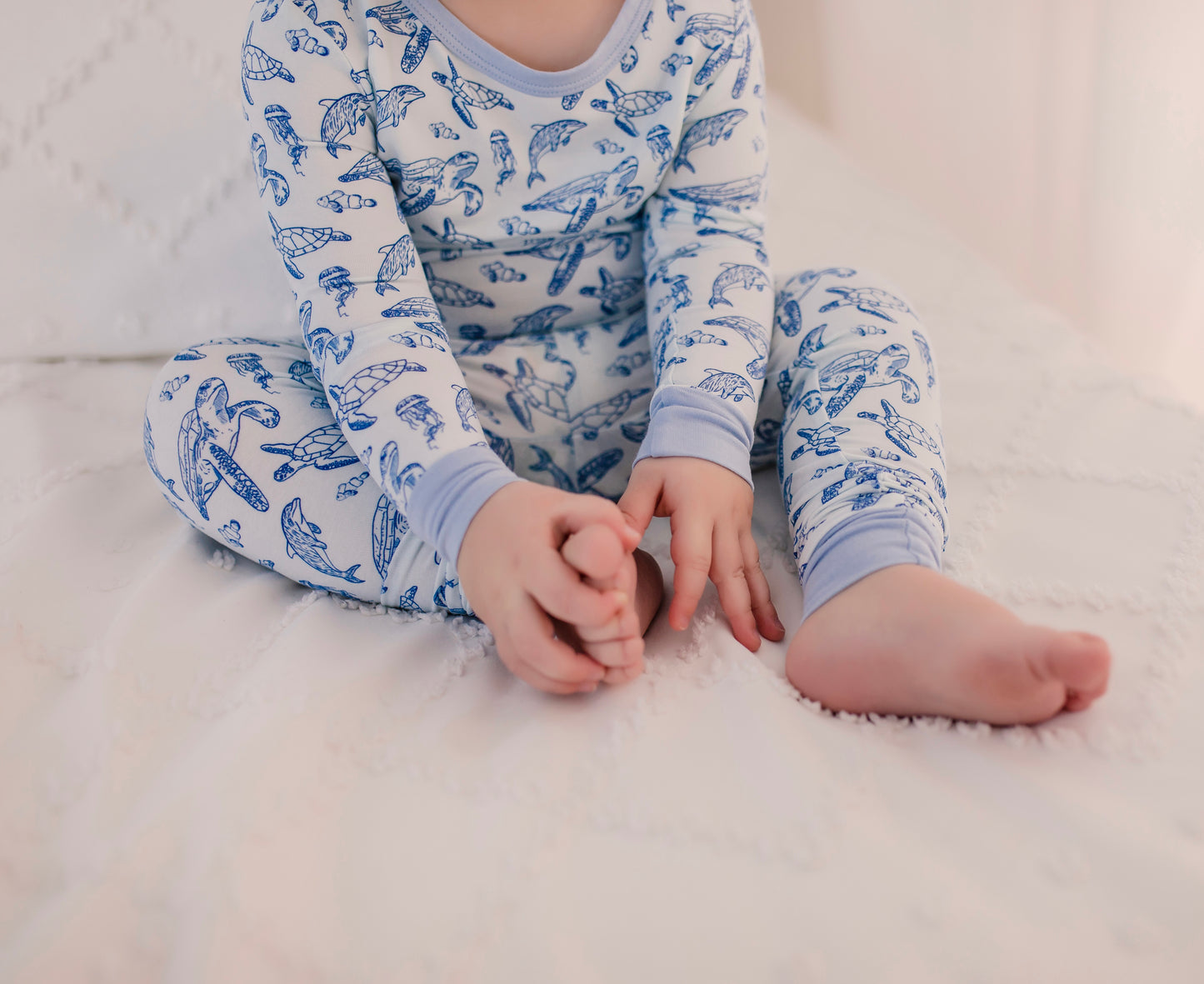 Child wearing long sleeve two piece pajama set with ocean animals such as sea turtles, dolphins, and jellyfish on a light blue background 