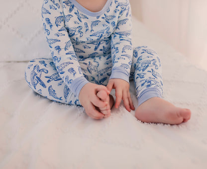 Child wearing long sleeve two piece pajama set with ocean animals such as sea turtles, dolphins, and jellyfish on a light blue background 
