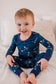A toddler wearing a two-piece pajama set with a dark blue background and gold constellation prints.