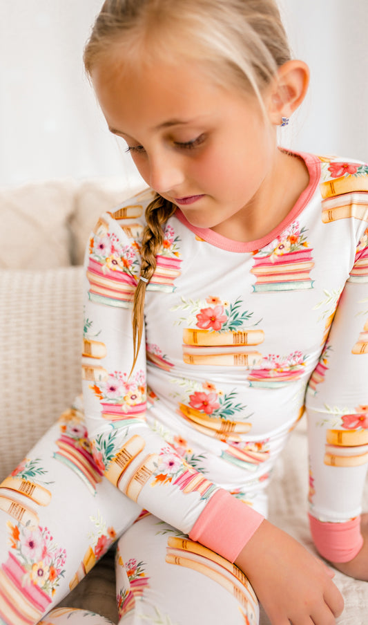 Girl wearing a colorful long-sleeve shirt and pants with floral and book patterns.