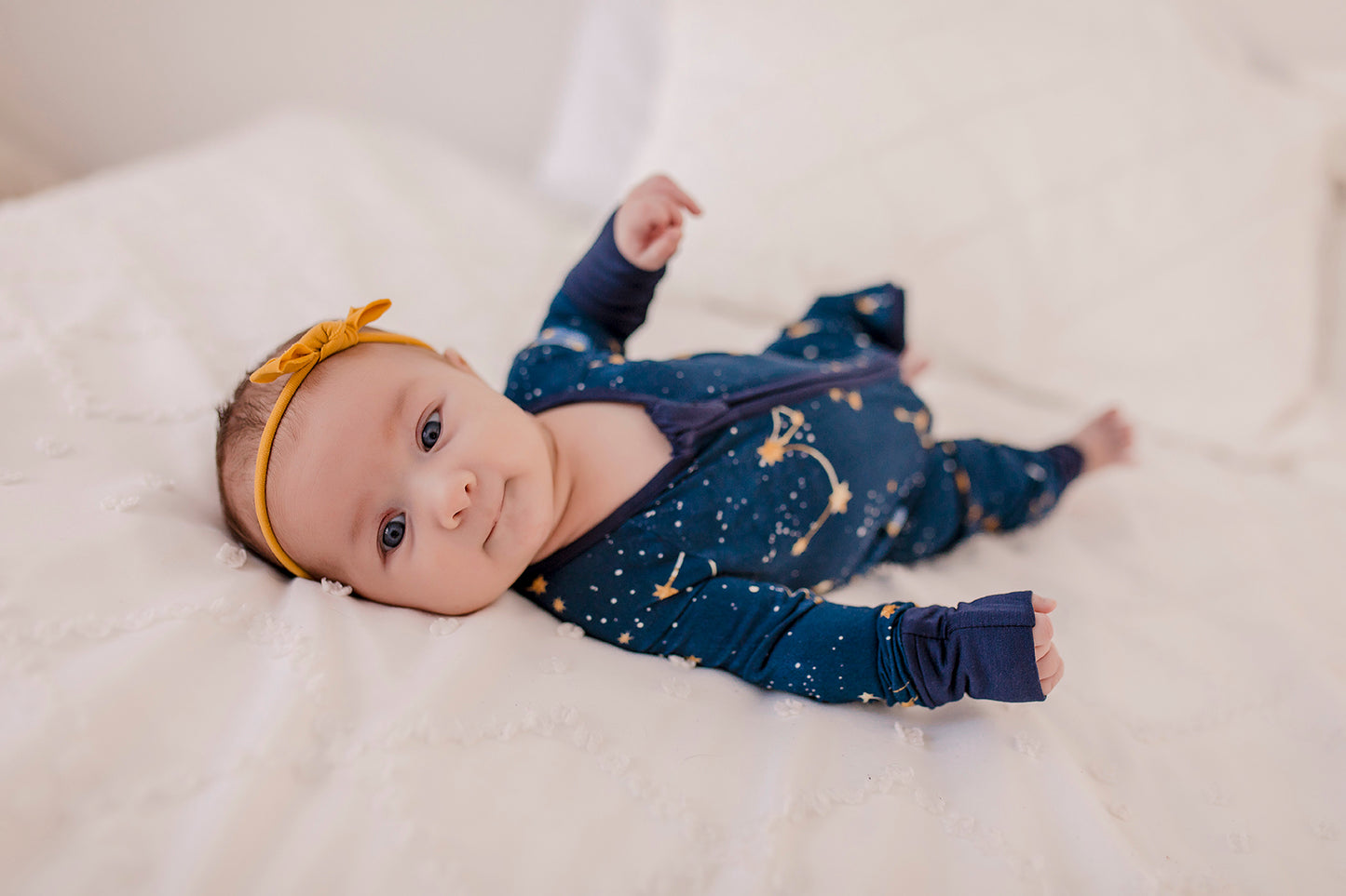 A baby wearing a dark blue zippy romper with a Maine September Sky that has the constellations of the little dipper and the big dipper 