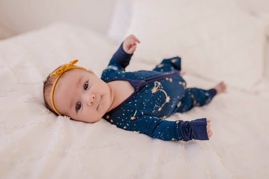 A baby wearing a dark blue zippy romper with a Maine September Sky that has the constellations of the little dipper and the big dipper 