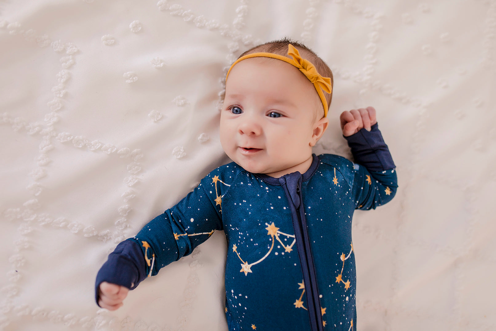 A baby wearing a dark blue zippy romper with a Maine September Sky that has the constellations of the little dipper and the big dipper 