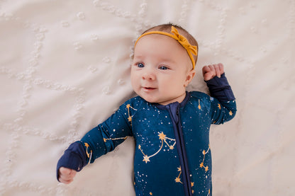 A baby wearing a dark blue zippy romper with a Maine September Sky that has the constellations of the little dipper and the big dipper 
