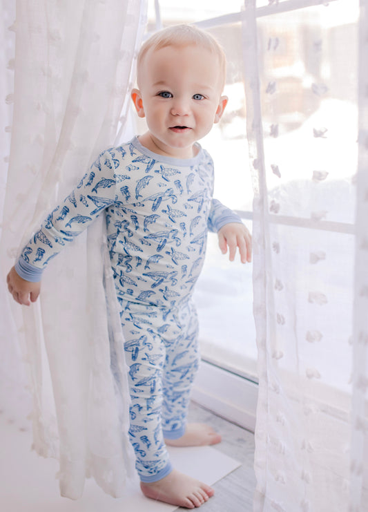 A toddler wearing a two-piece pajama set with a pattern that includes sea turtle and dolphin designs