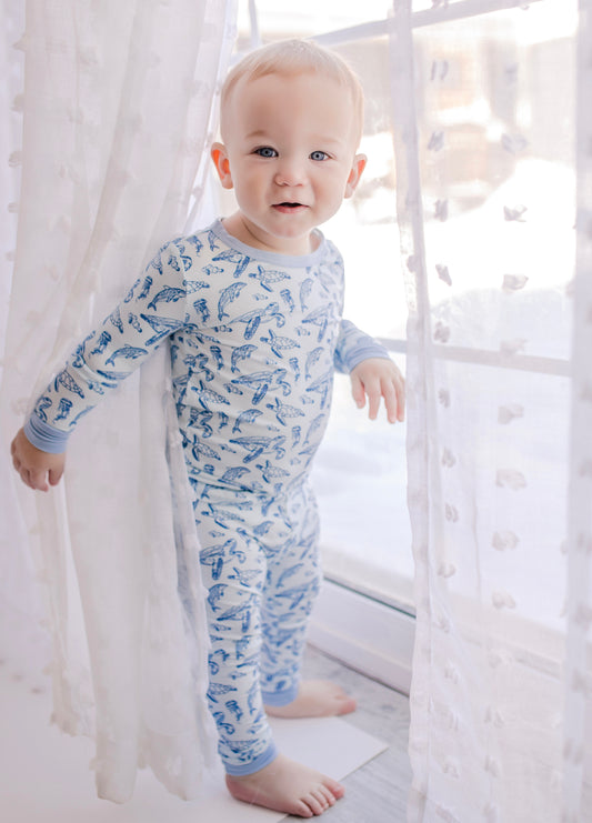 A toddler wearing a two-piece pajama set with a pattern that includes sea turtle and dolphin designs