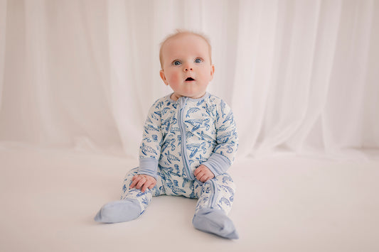 A baby wearing a long-sleeved romper with an ocean animal pattern that has sea turtles, dolphins, and jellyfish, in shades of blue