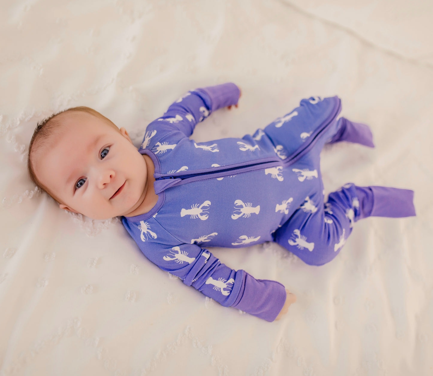 Child wearing a purple zippy romper with white Maine lobster pattern and purple cuffs 