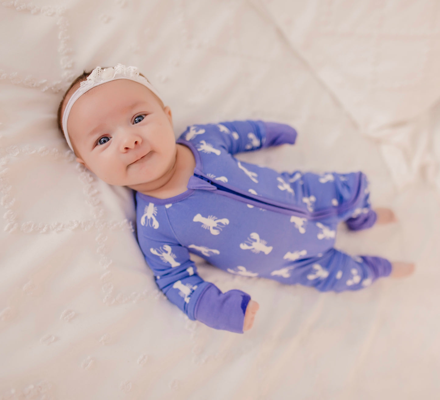 A baby wearing a purple zippy romper with a white lobster design
