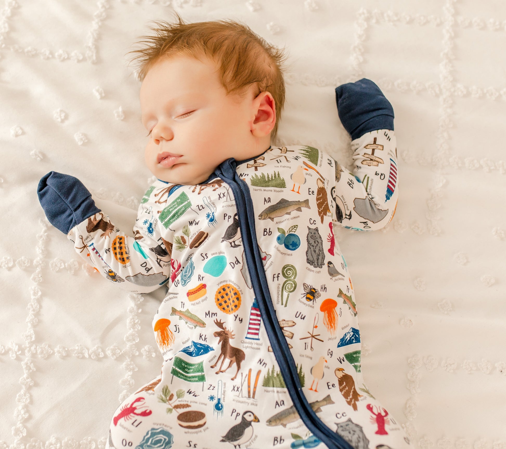 Child wearing pajamas with nature-themes, food themes, animal themes, and ocean themes to make up every letter of the Maine alphabet 