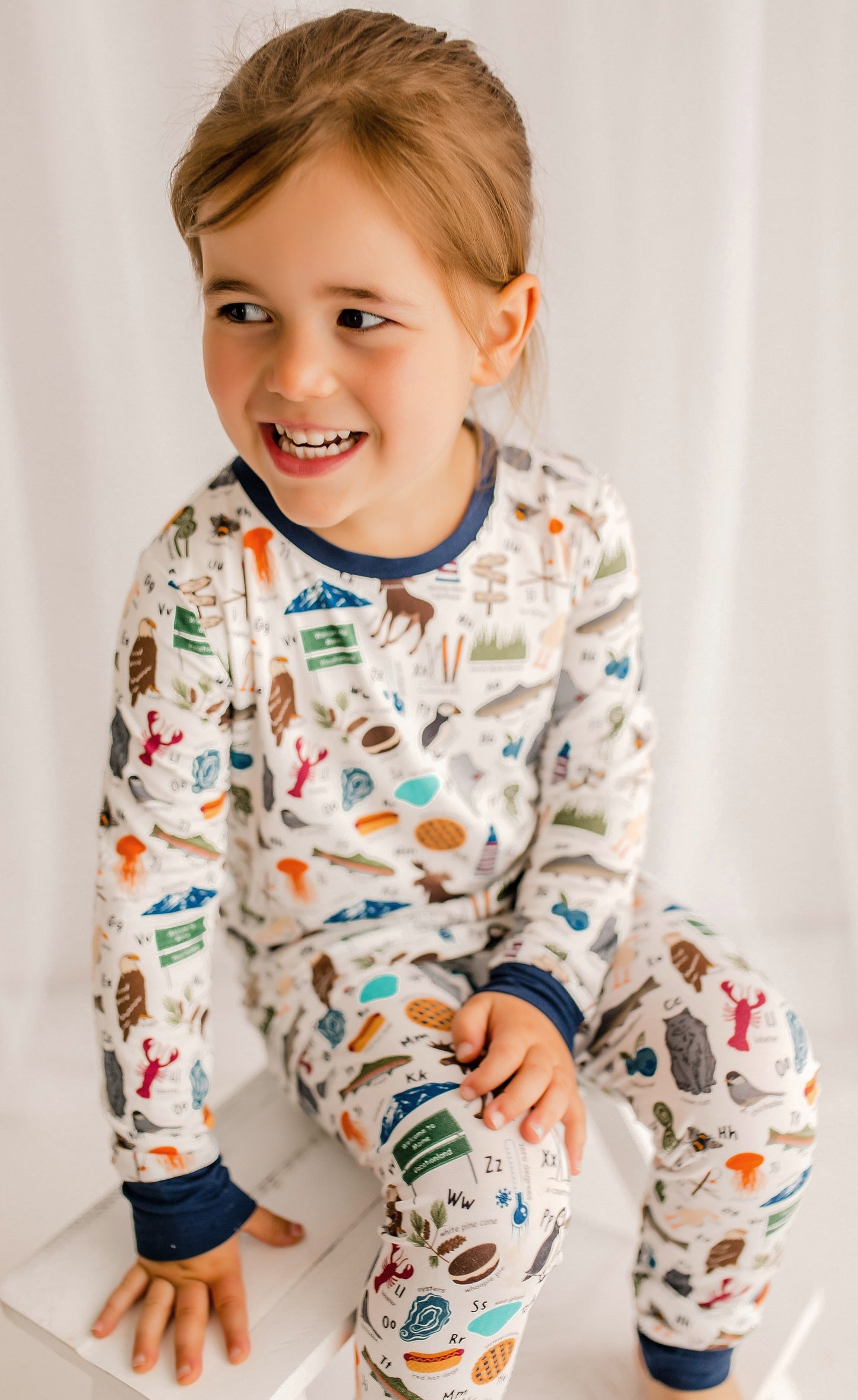 Child wearing a white background with all kinds of items from lobsters and blueberries to waffles and eagles, to each represent a letter of the alphabet 