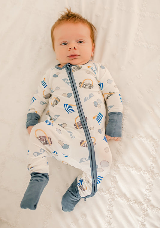 Baby in a onesie with clam diggers, baskets, clams, and waves. 