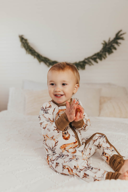 A baby wearing a white bamboo romper with a deer design with antlers and brown accents