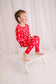 Child wearing coastal maine themed pajamas with long sleeves and pants on a red background with white lobster pattern 