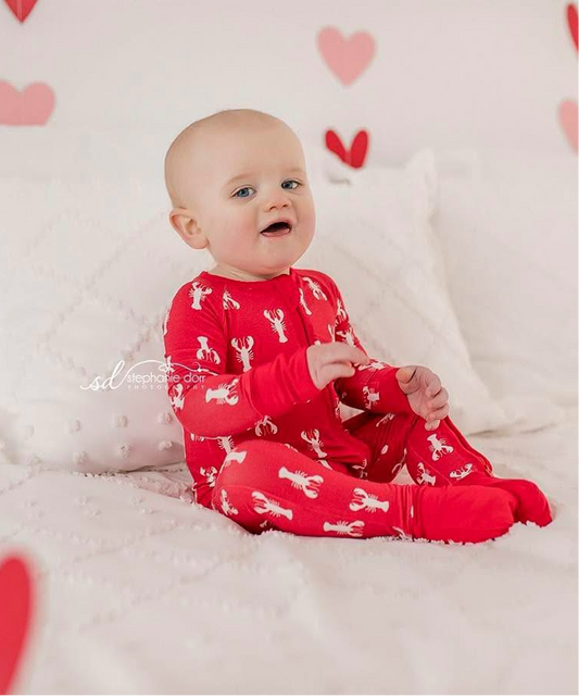 A baby wearing a red zippy romper with white lobsters 