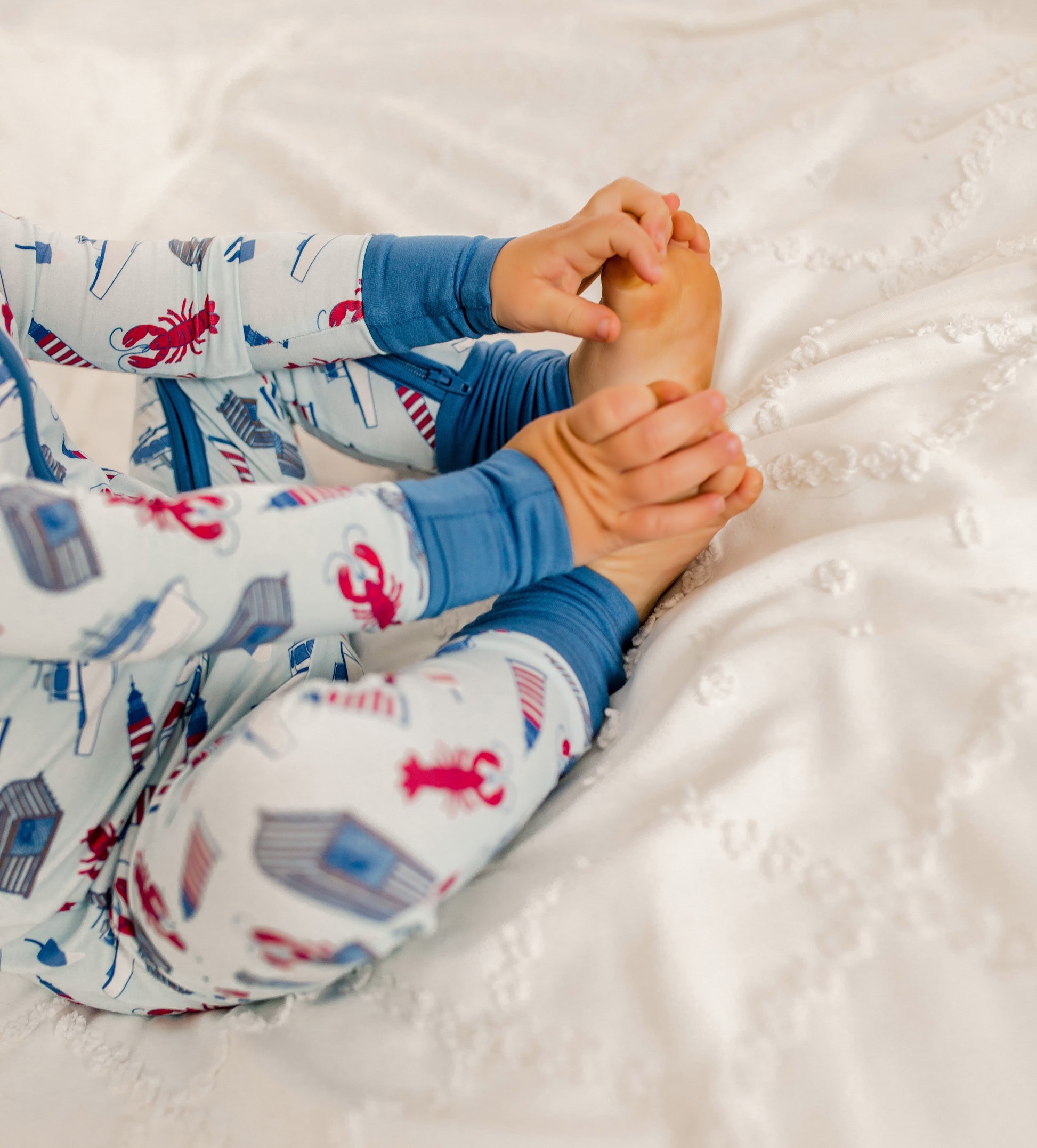 Child wearing a light blue one piece with maine lobsters, traps, buoys, and boats with lighthouses and darker blue cuffs 
