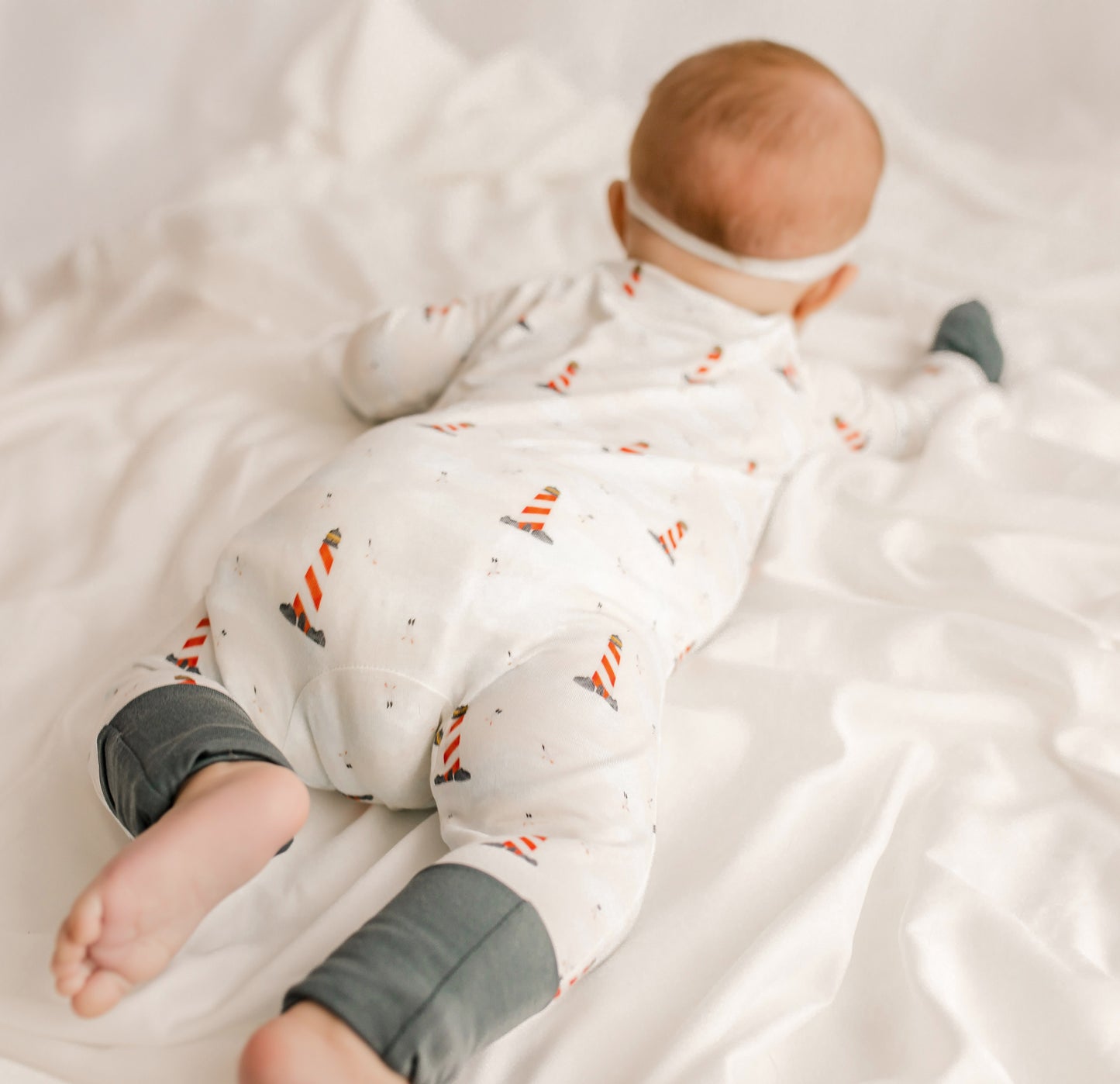 Baby wearing white one piece with black cuffs and lighthouses in red and white and black all over 