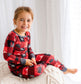 Child wearing red and black pajamas with moose and tree patterns and gray accents 