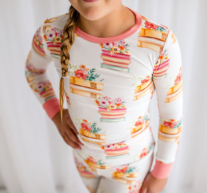 Child wearing a long-sleeve pajama set with colorful books and and array of flowers on a white background with pink accents