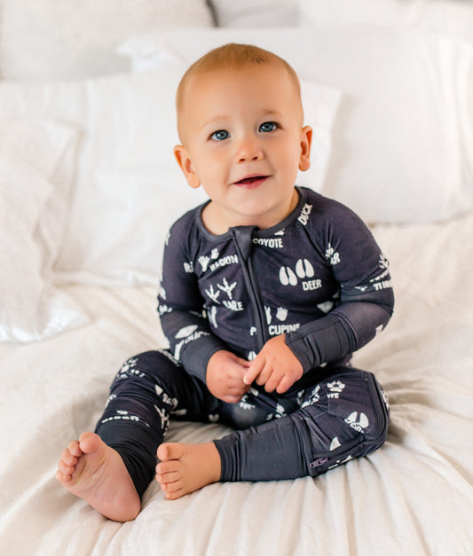 Baby wearing a dark gray bamboo onesie with white patterns and lettering sitting on a white blanket.