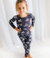 Child standing wearing dark gray two piece pajamas with white animal prints and lettering with a white background