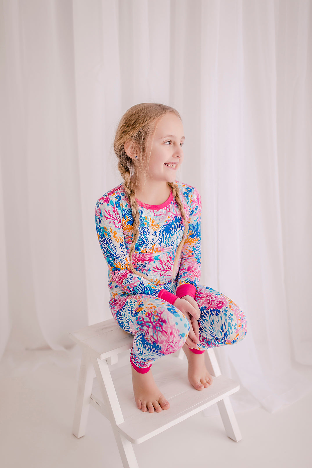 Child wearing Maine coral reefs with a white background with coral reefs in all different shades of pink, blue and white with pink cuffs. 