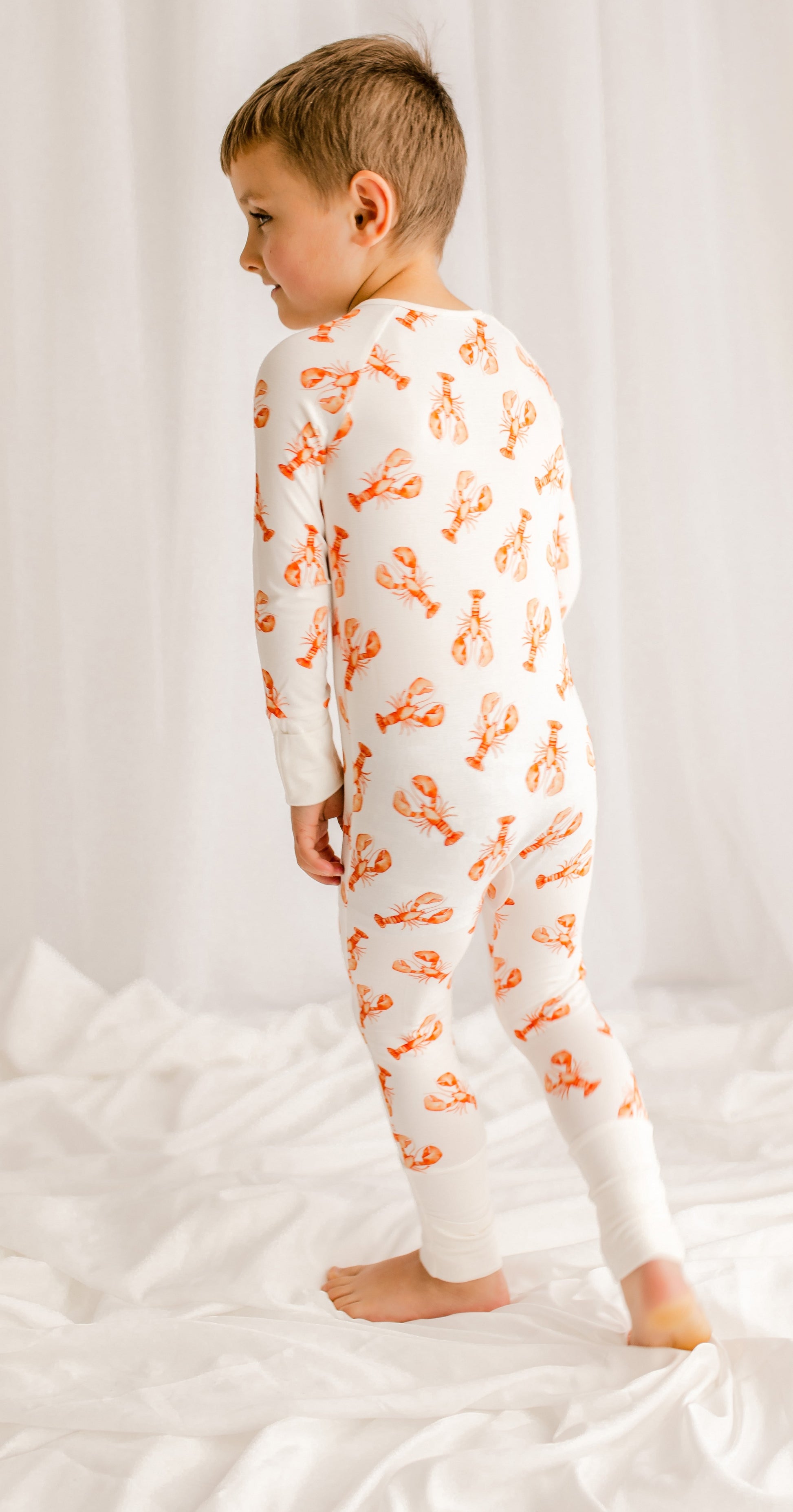 Child wearing a white onesie with orange maine lobster patterns 