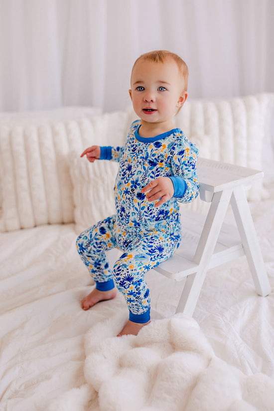 Baby in blue floral pajamas standing on a white bed.