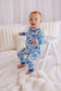 Baby in blue floral pajamas standing on a white bed.