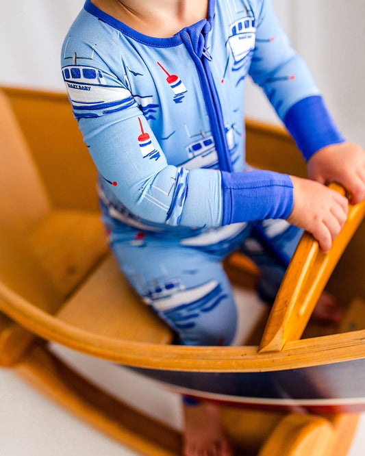 Child wearing a blue one piece watercolor with lobster boats, buoys, waves, and seagulls 