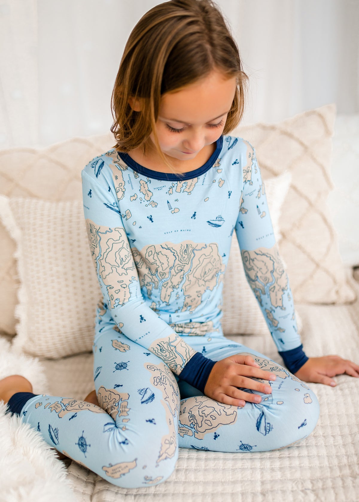 Child wearing a blue two piece pajama set with a nautical map of a part of the Maine coastline and the Atlantic Ocean. 