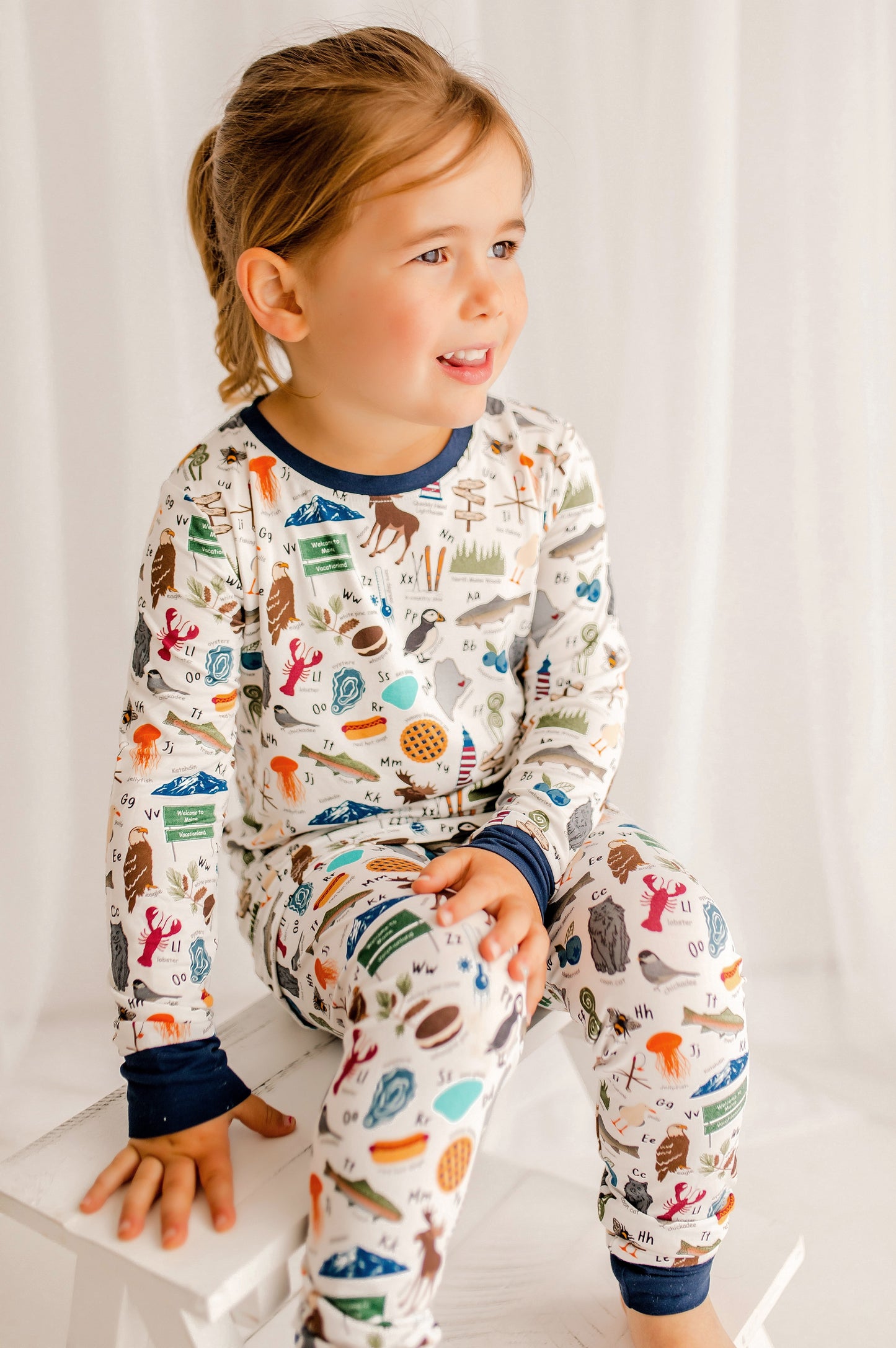 Child wearing pajamas with a pattern of animals, lobsters, fish, and more that all represent Maine for every letter of the alphabet 