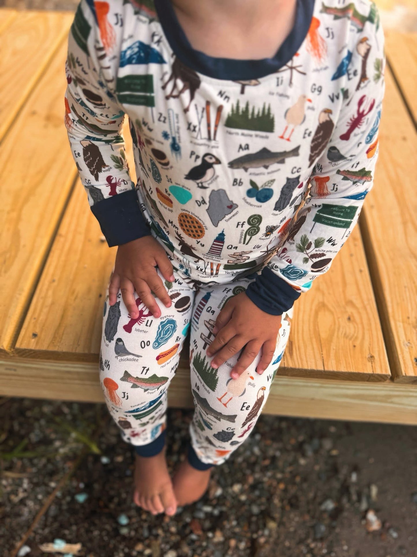 Child wearing pajamas with nature-themes, food themes, and animal themed to make up the Maine alphabet 