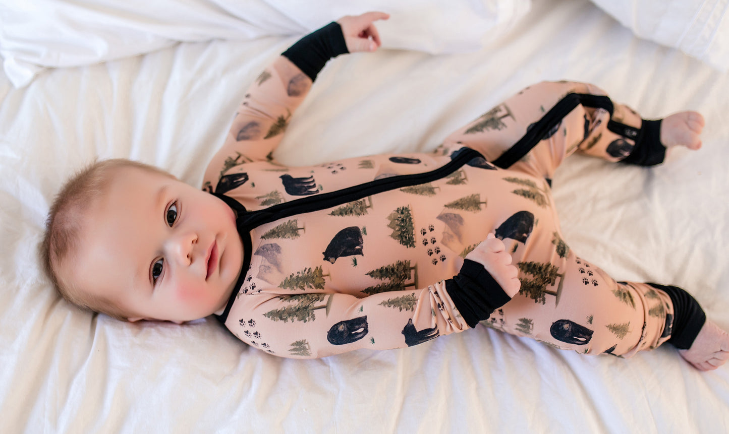 Baby wearing a tan onesie with black bears along with their tracks, mountains, and trees from the Maine wilderness 