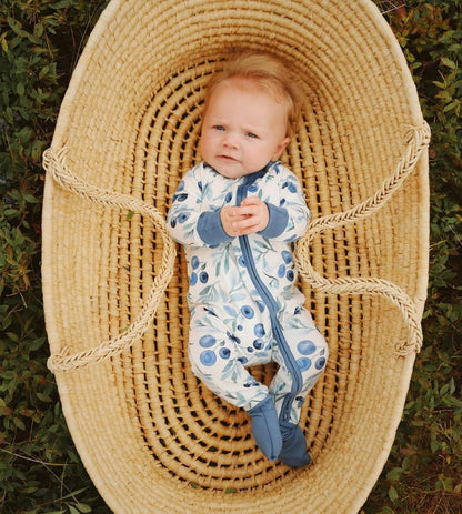 Baby wearing a white one piece pajama with maine blueberries with different shades of blue throughout the pajamas 