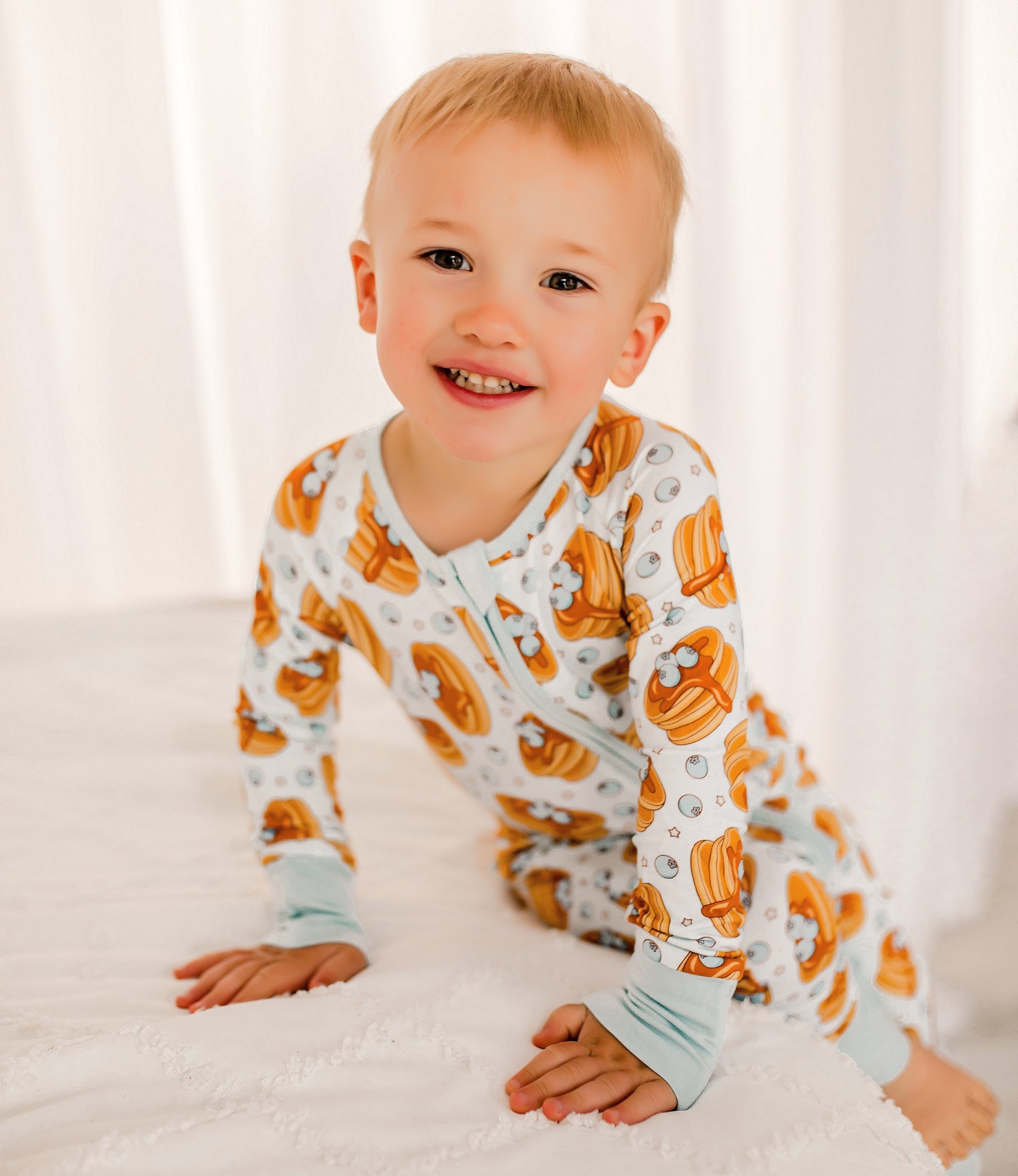 Maine blueberry stacked pancakes with syrup on a light blue background with light blue cuffs with cream colored little stars 